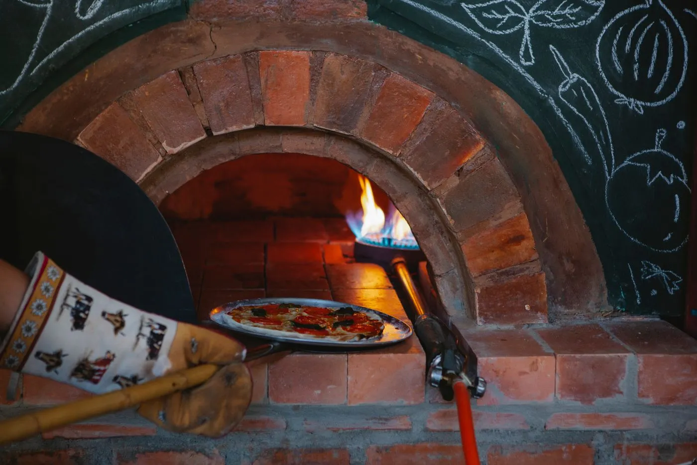 Une pizza enfournée à la pelle dans un four à bois en brique