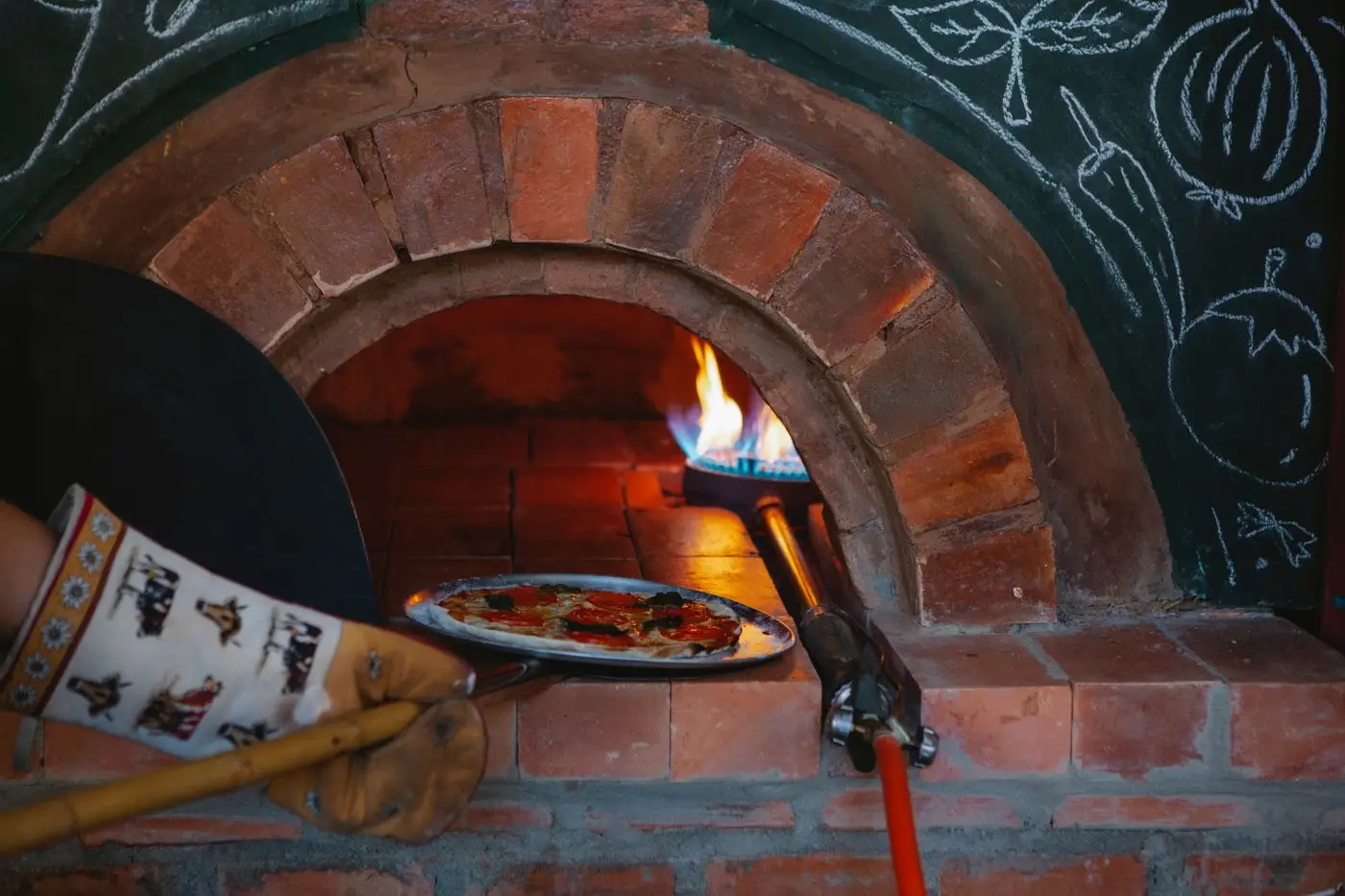 Une pizza enfournée à la pelle dans un four à bois en brique